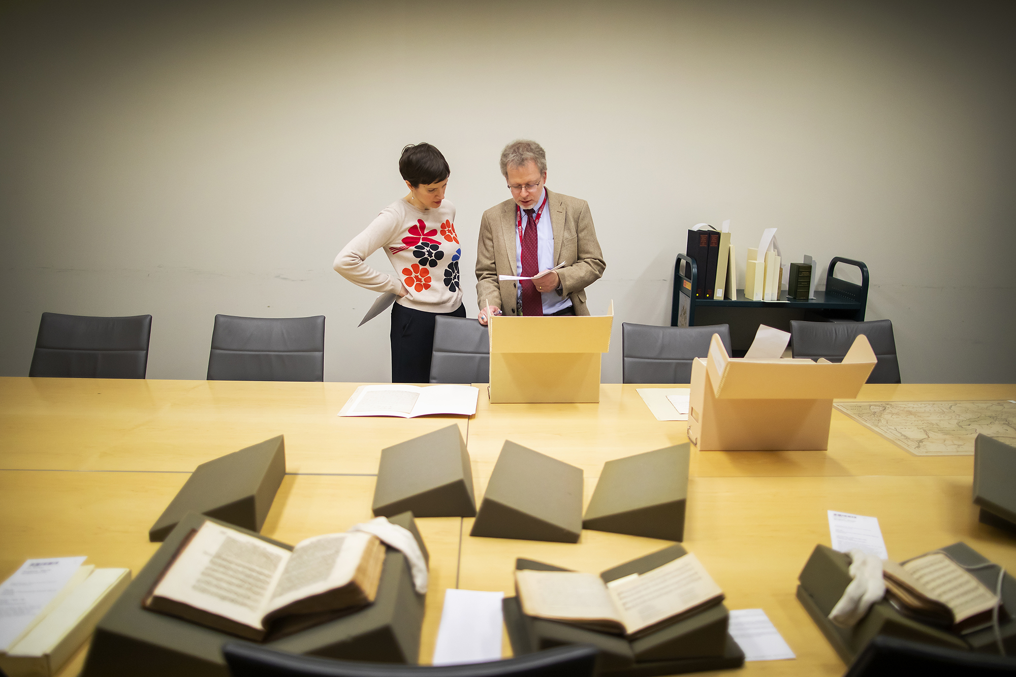 Two people looking at a text with several books laid out on a table in front of them.