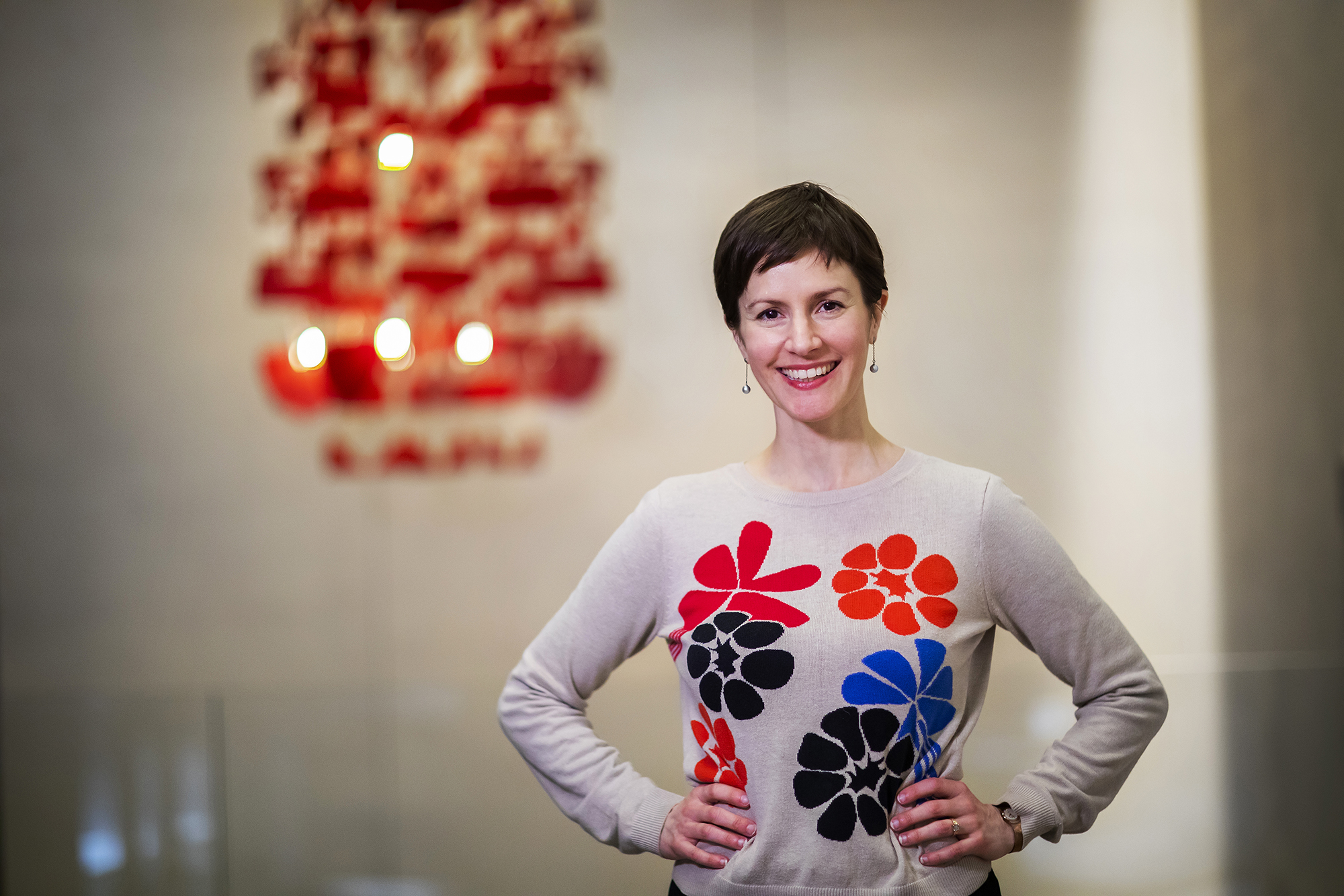 Professor standing with hands on her hips in the library with a chandelier in the background