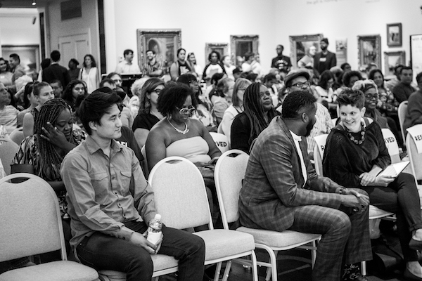 A room full of people seated with others standing in the back of the room