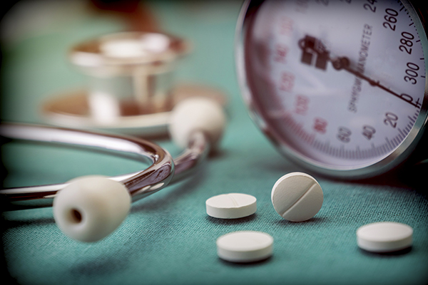 closeup of prescription pills on a surface beside a stethoscope and blood pressure gauge