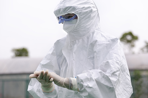Person wearing full protective gear including latex gloves, goggles, hood and full protective medical gown.