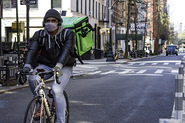 Bike food delivery courier wearing a protective face mask while riding through NYC empty streets
