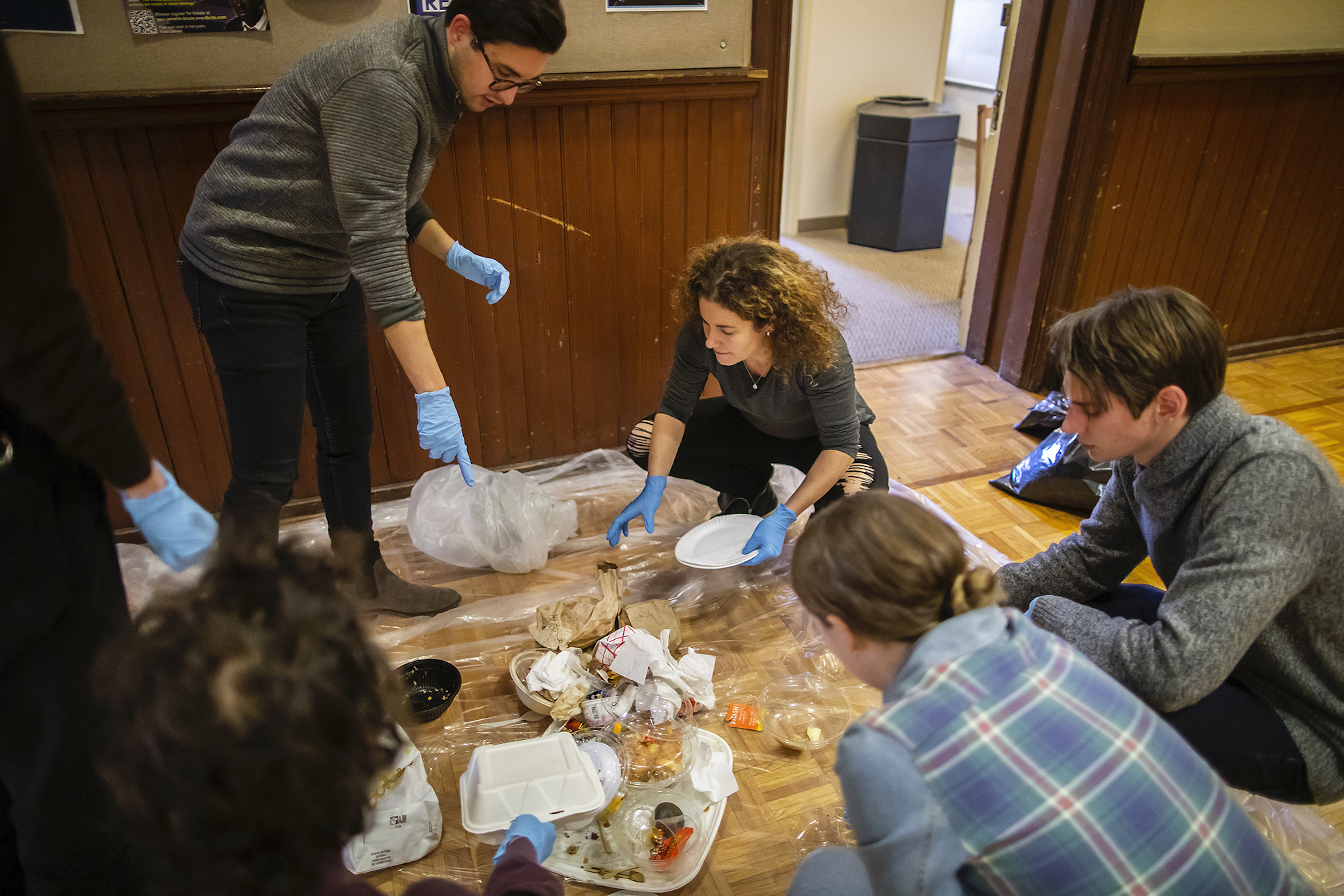 People wearing latex gloves crouch on the floor around a pile of garbage