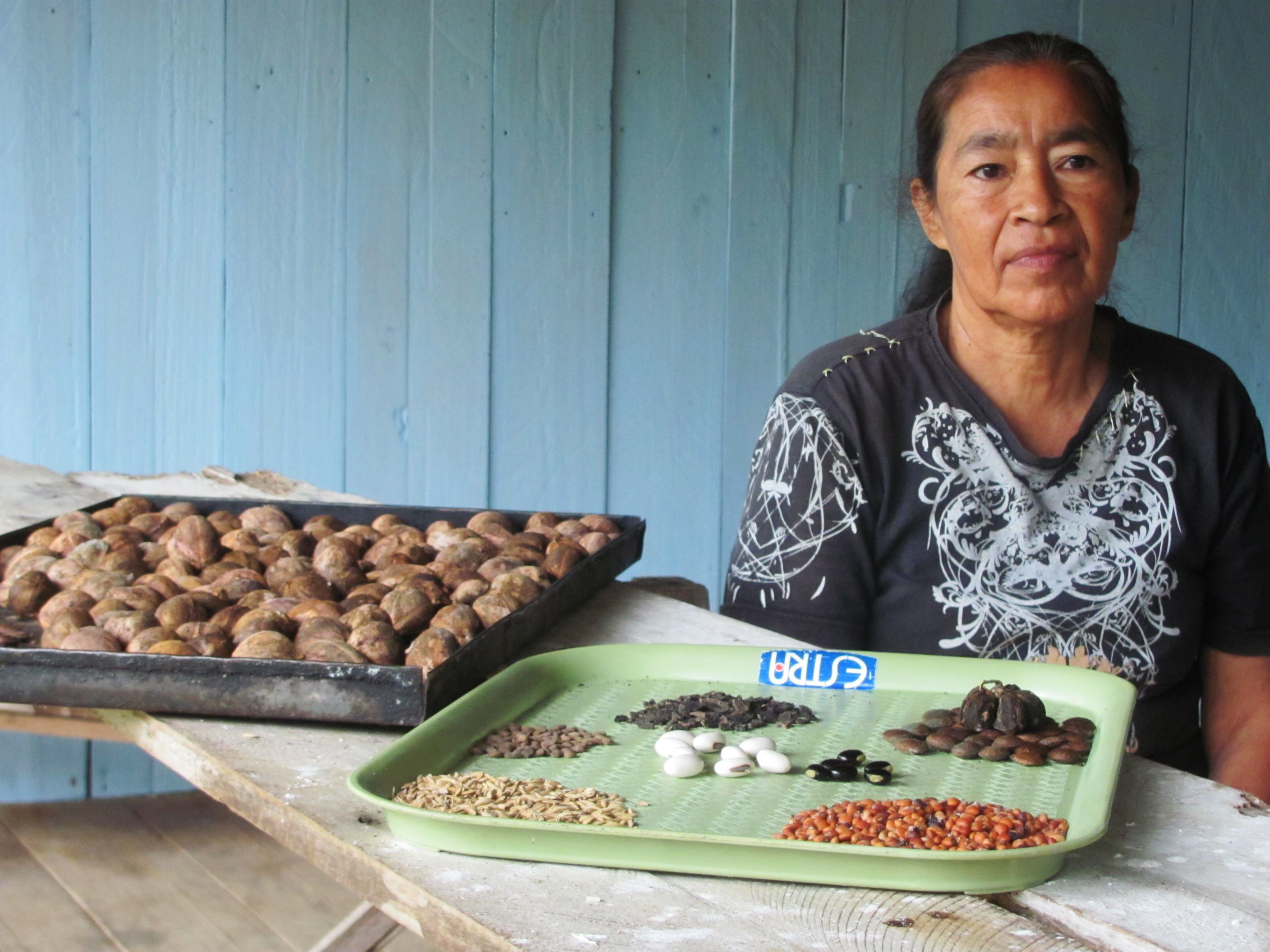 A woman sits behind a wooden table with two trays of different seed varieties. 