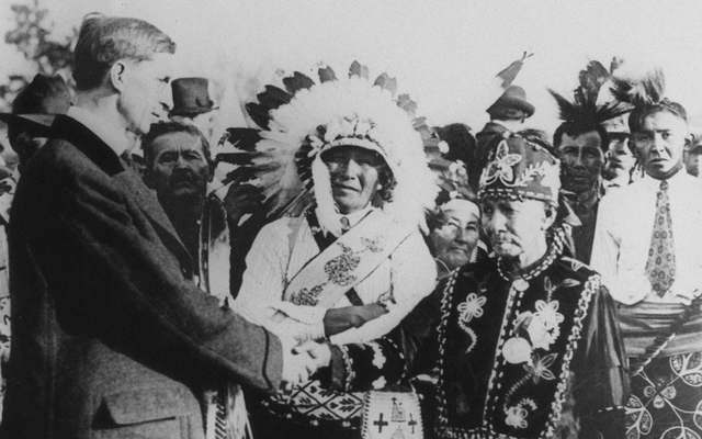 Man shakes hands with member of Ojibwe tribe of Wisconsin, an another man in headdress looks on.