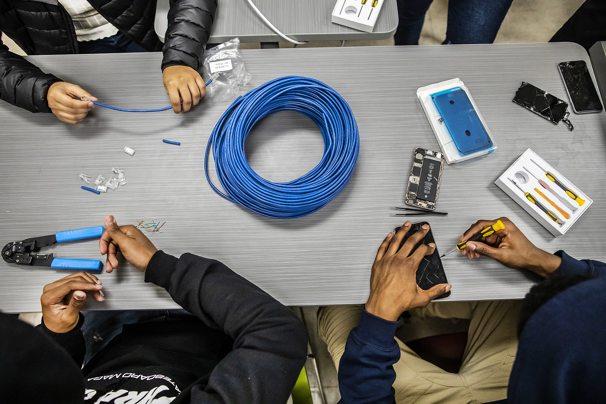 A flat shot of students' hands working on mobile phones and ethernet cords