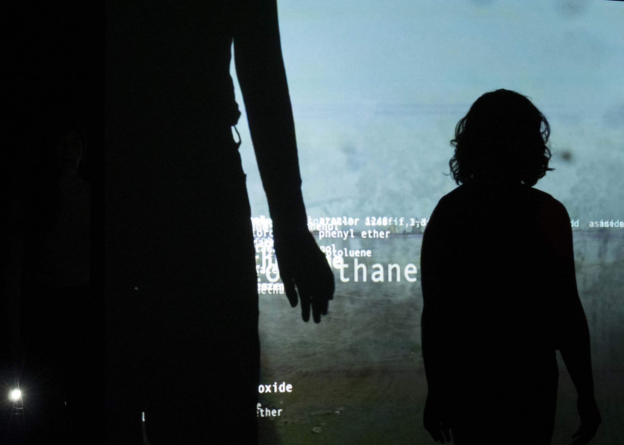 Silhouettes of two people in front of a blue background displaying chemical names