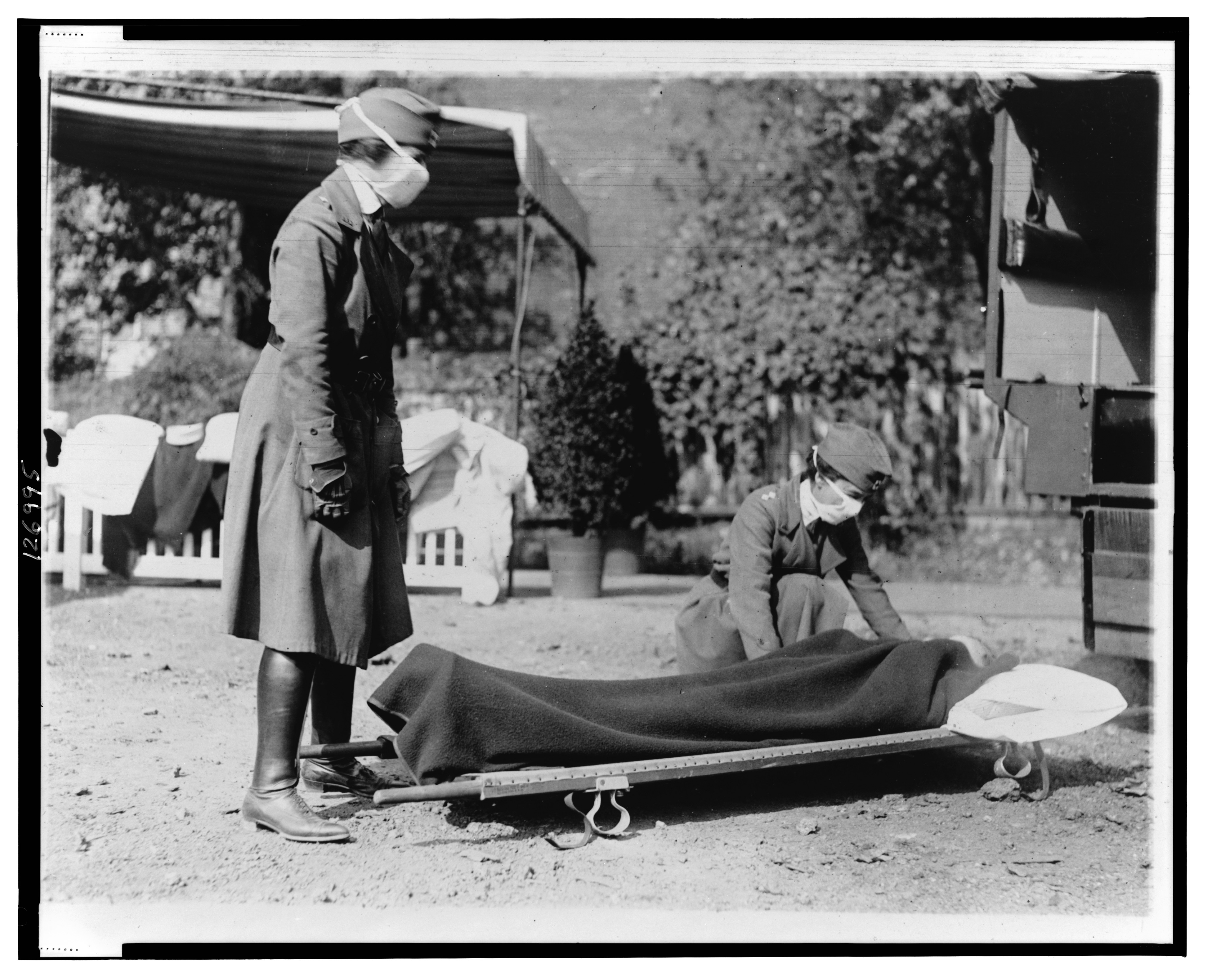 Two masked nurses tend to a stretcher outside