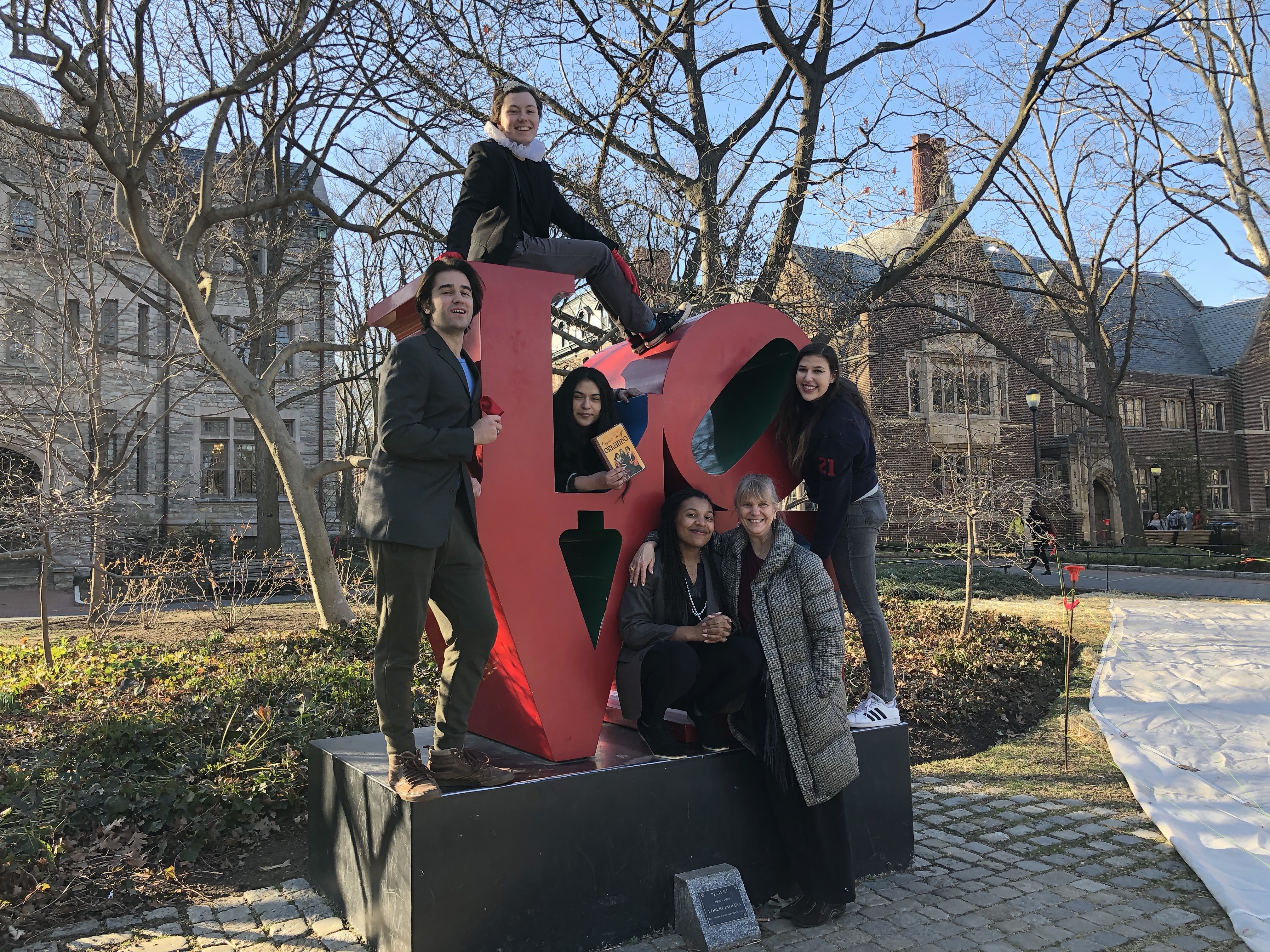 Five students and a professor sitting on the LOVE statue on Penn's campus.