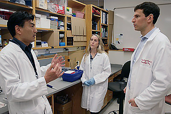  Taku Kambayashi, Ruth-Anne Langan Pai, and David Fajgenbaum stand talking in a lab.