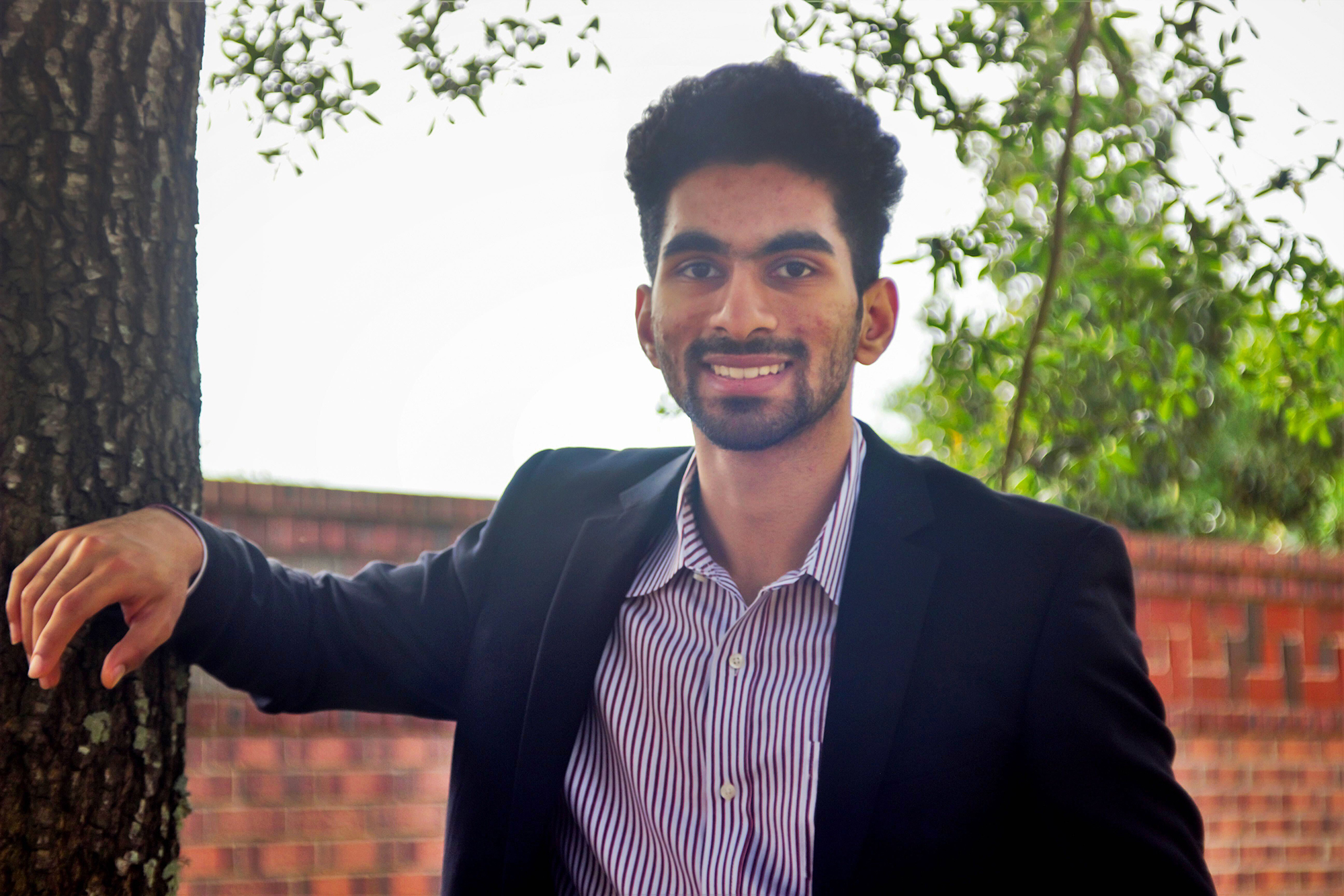 Nikil Ragav smiles and leans casually on a tree