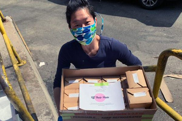 One of the founders of Off Their Plate wearing a face mask holding a box full of meals