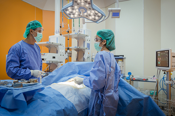 Two medical professionals in scrubs perform surgery in an operating room.