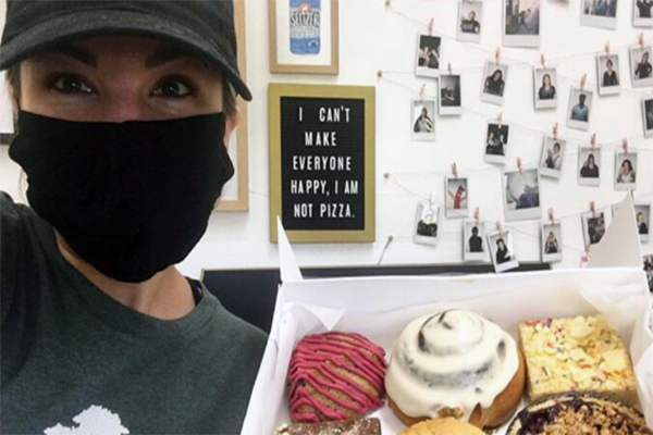 Selfie of a person wearing a face mask holding up a box of vegan pastries in their bakery