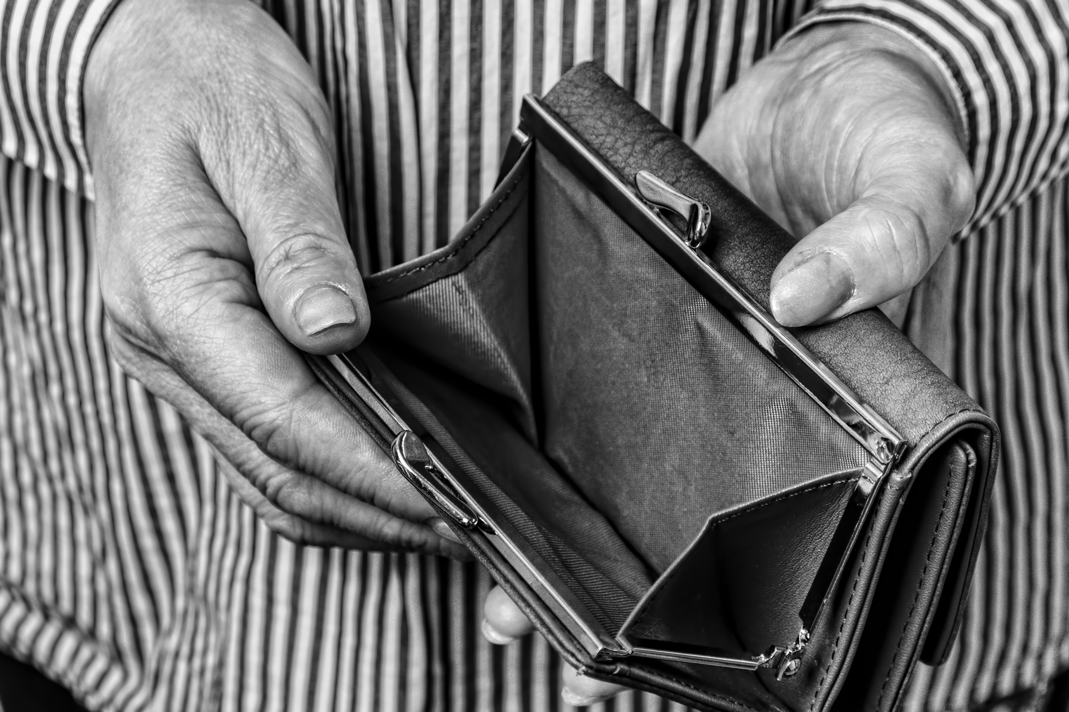 Black and white images of hands of an older person holding open an empty change purse of a wallet.