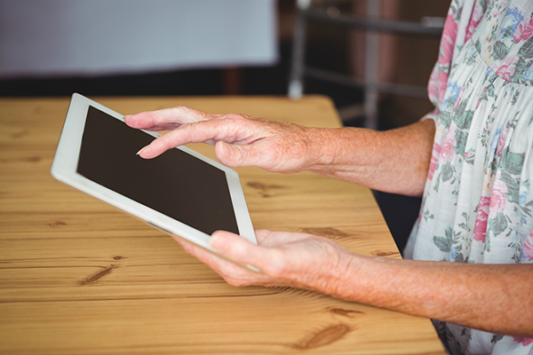 An elderly person’s hands holding a iPad.