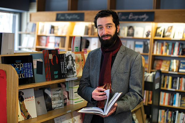 Ahmad Almallah stands in a bookstore holding a book.