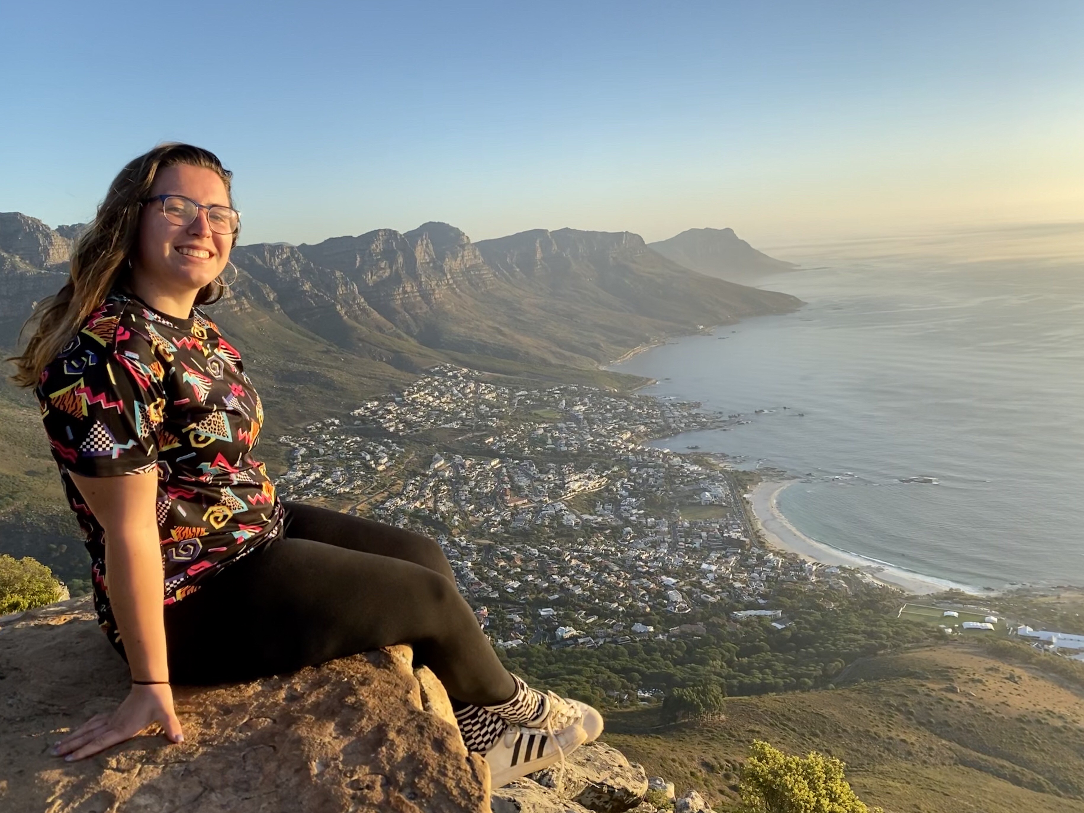 Smiling person sites on high ledge overlooking a coastal city