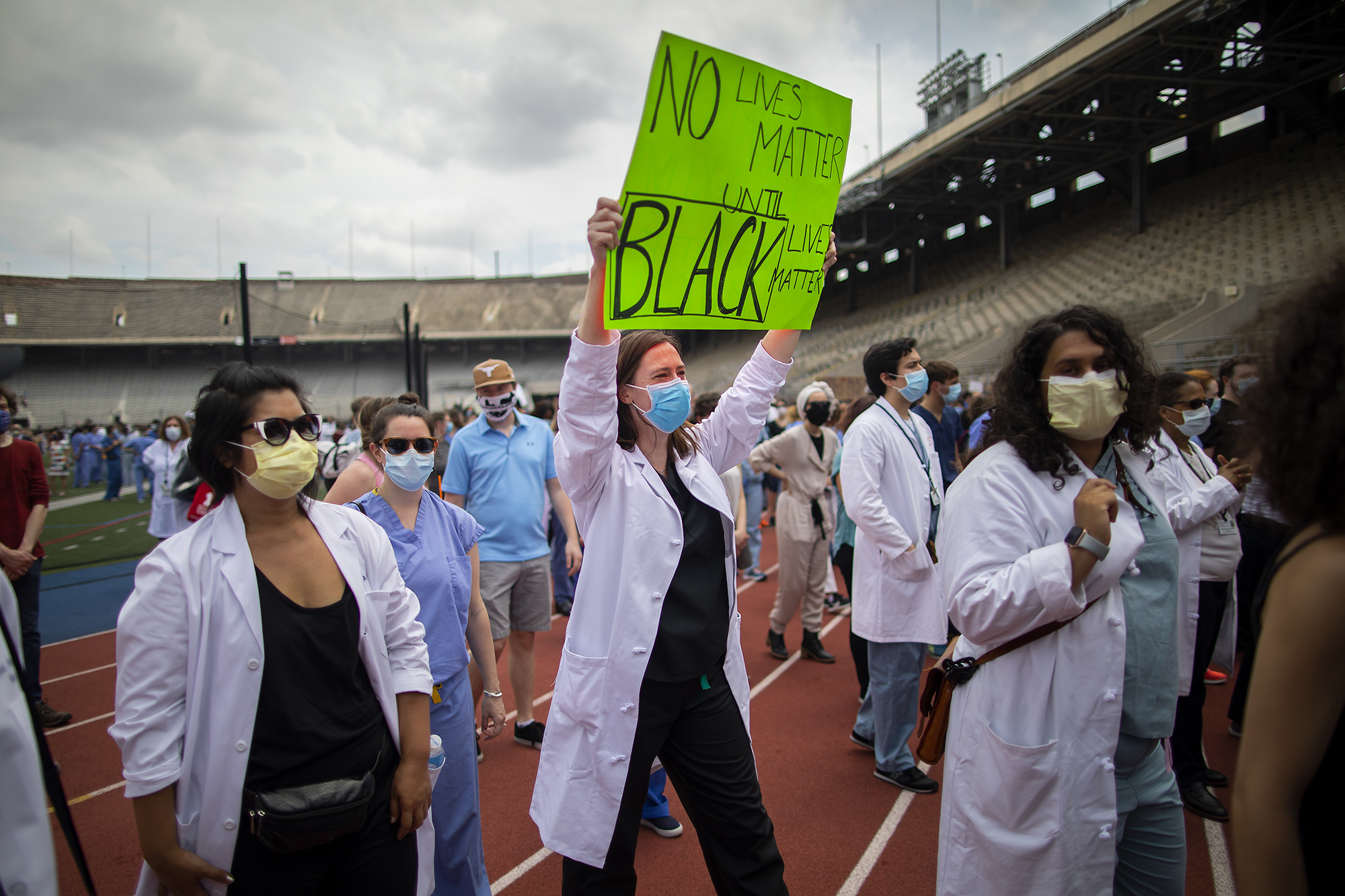 Penn Medicine workers in protective face masks stand on the track at Franklin Field, one holds a sign that reads NO Lives Matter until BLACK Lives Matter.