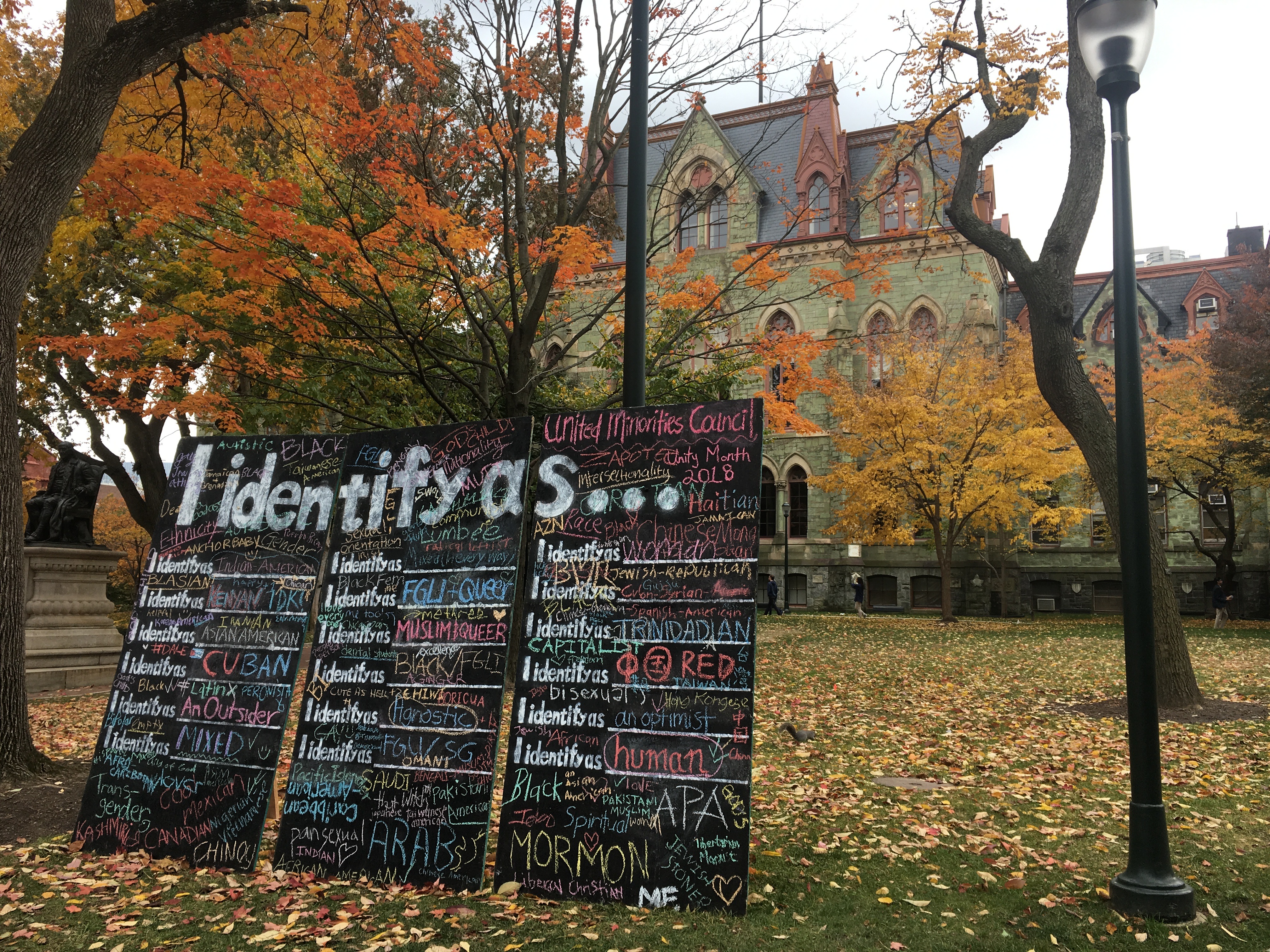 Three blackboards in front of Claudia Cohen Hall say "I identify as..." with various descriptors written in colorful chalk (mormon, human, FGLI, queer, etc)