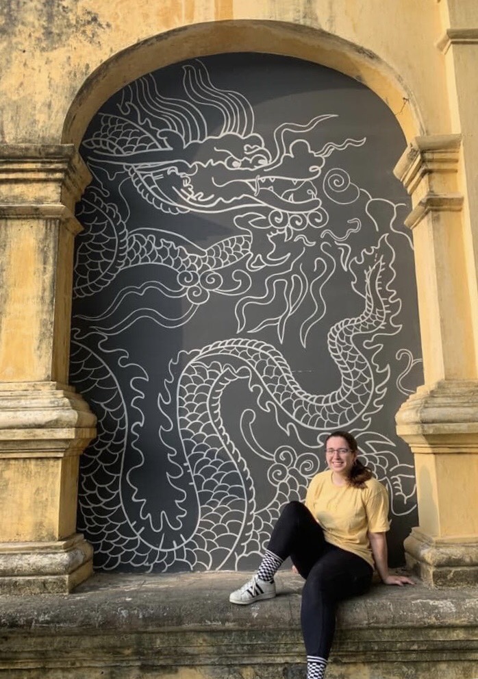 Person poses in front of a mural set in between columns