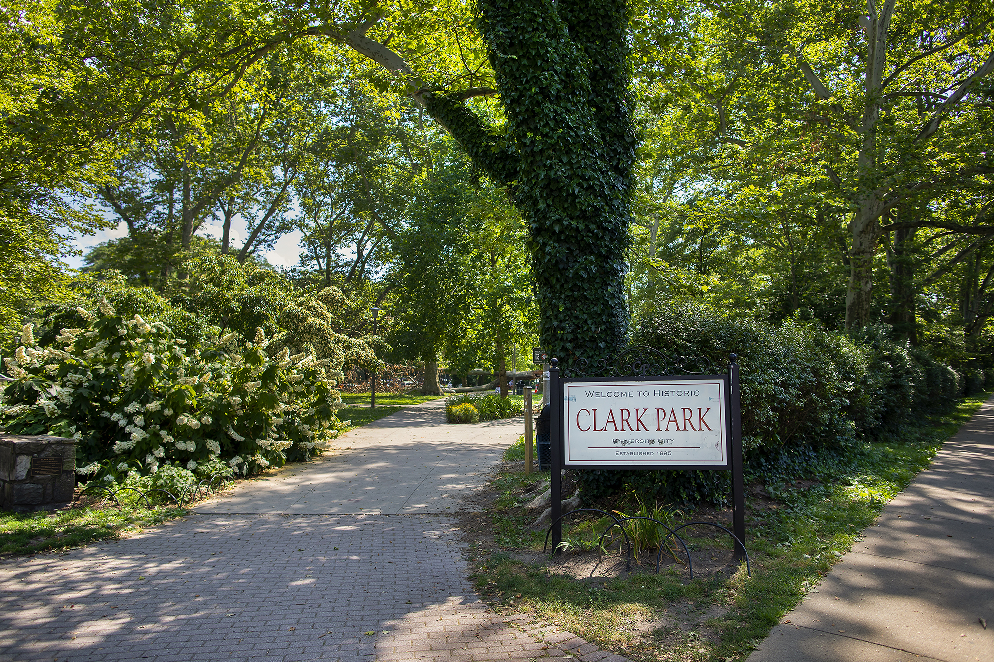 Landscape photo of a park, with a sign that reads "Welcome to Historic Clark Park, University City, Established 1895"