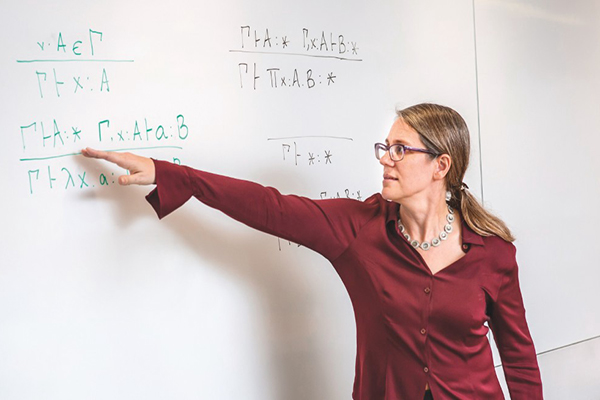 Stephanie Weirich stands pointing to a mathematical equation at a whiteboard.