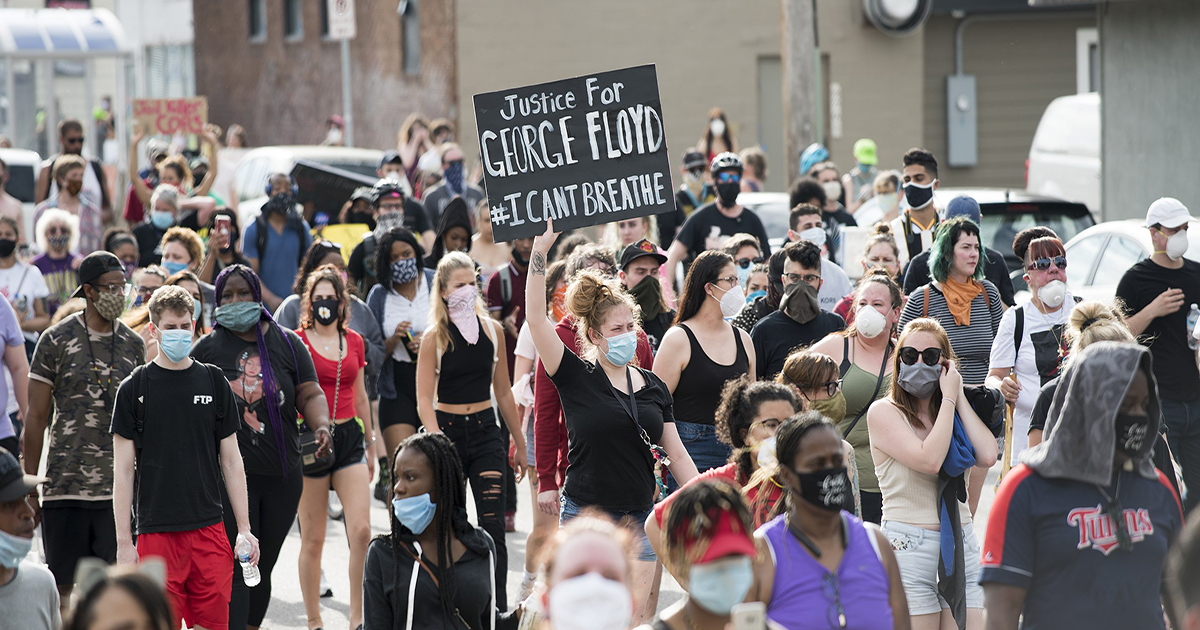 Crowd of people march in street, one person in the center holding sign reading "Justice for George Floyd"