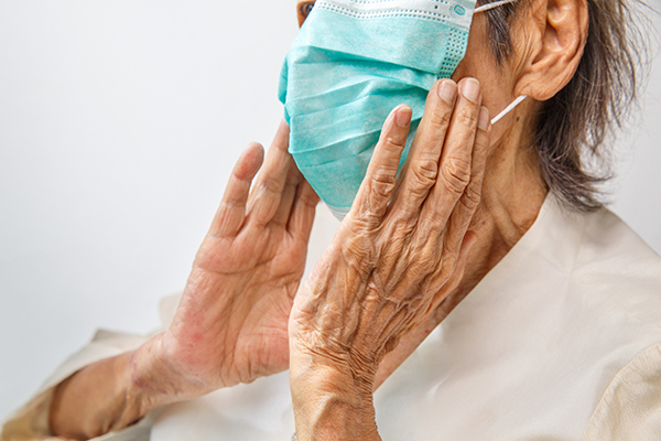 Elderly person holds their hands to their face wearing a medical face mask.