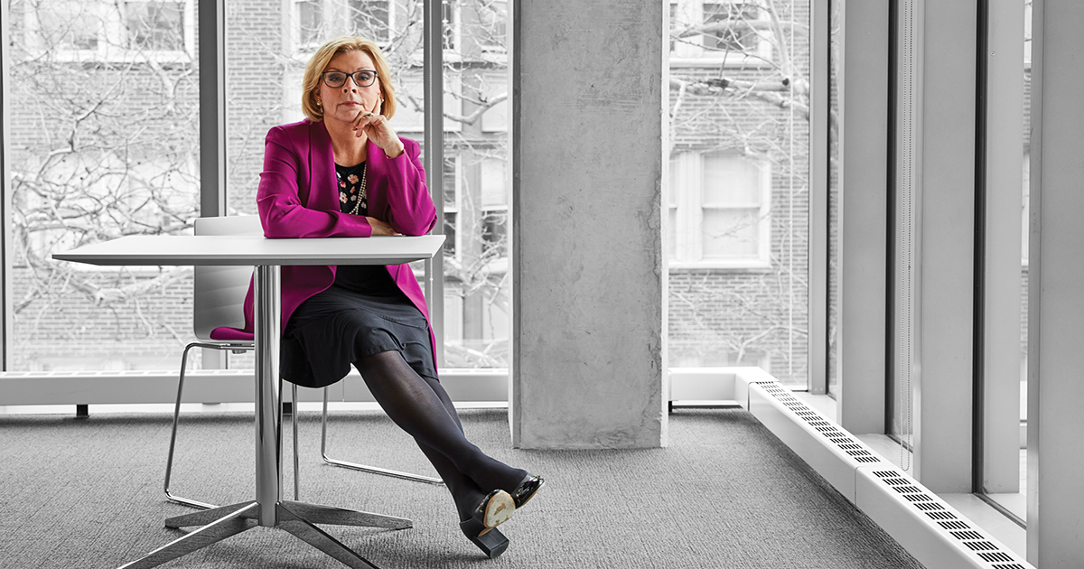 Marci Hamilton sits at a table beside large windows overlooking Penn campus.