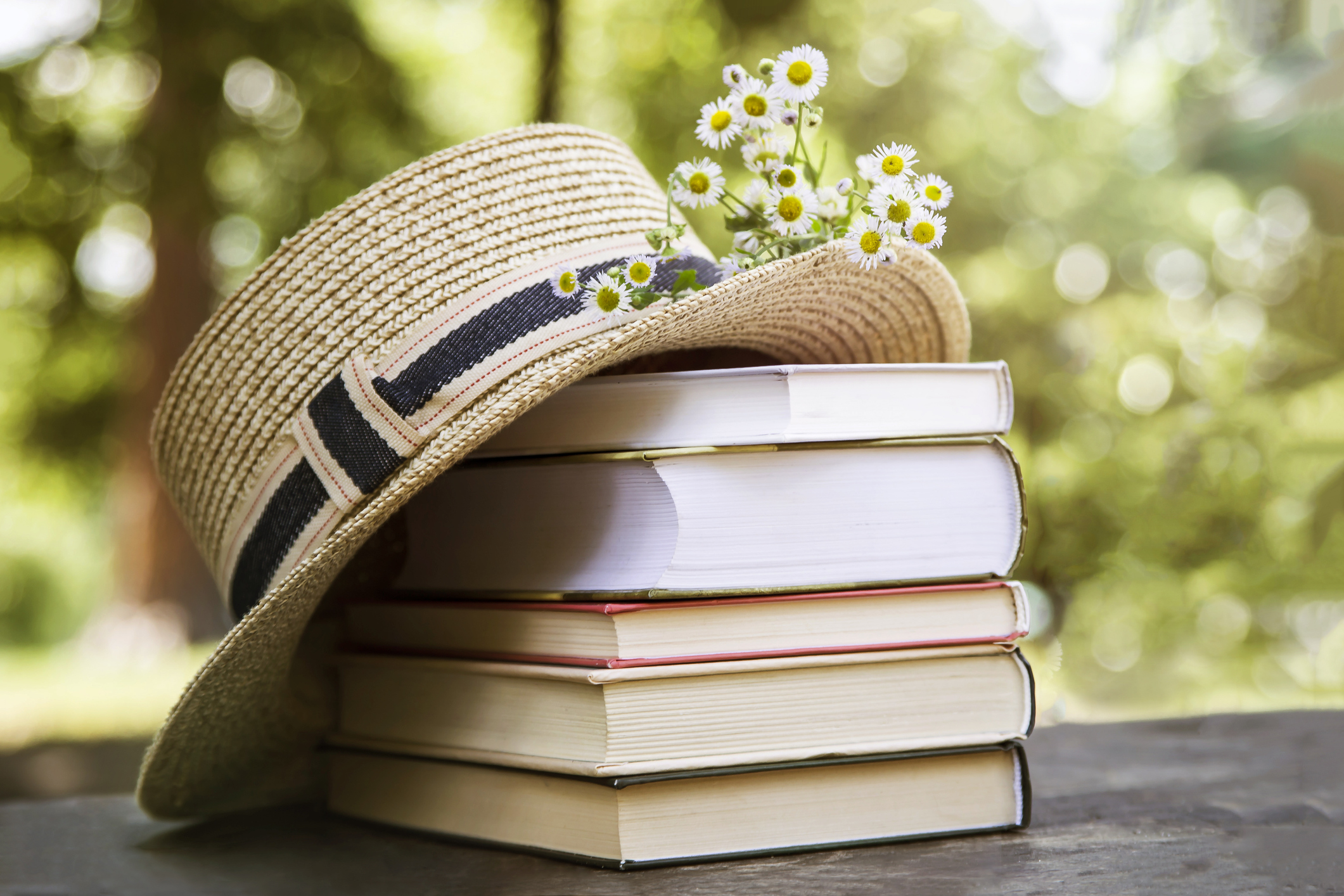 Stack of books outdoors with a hat and flowers on top of them