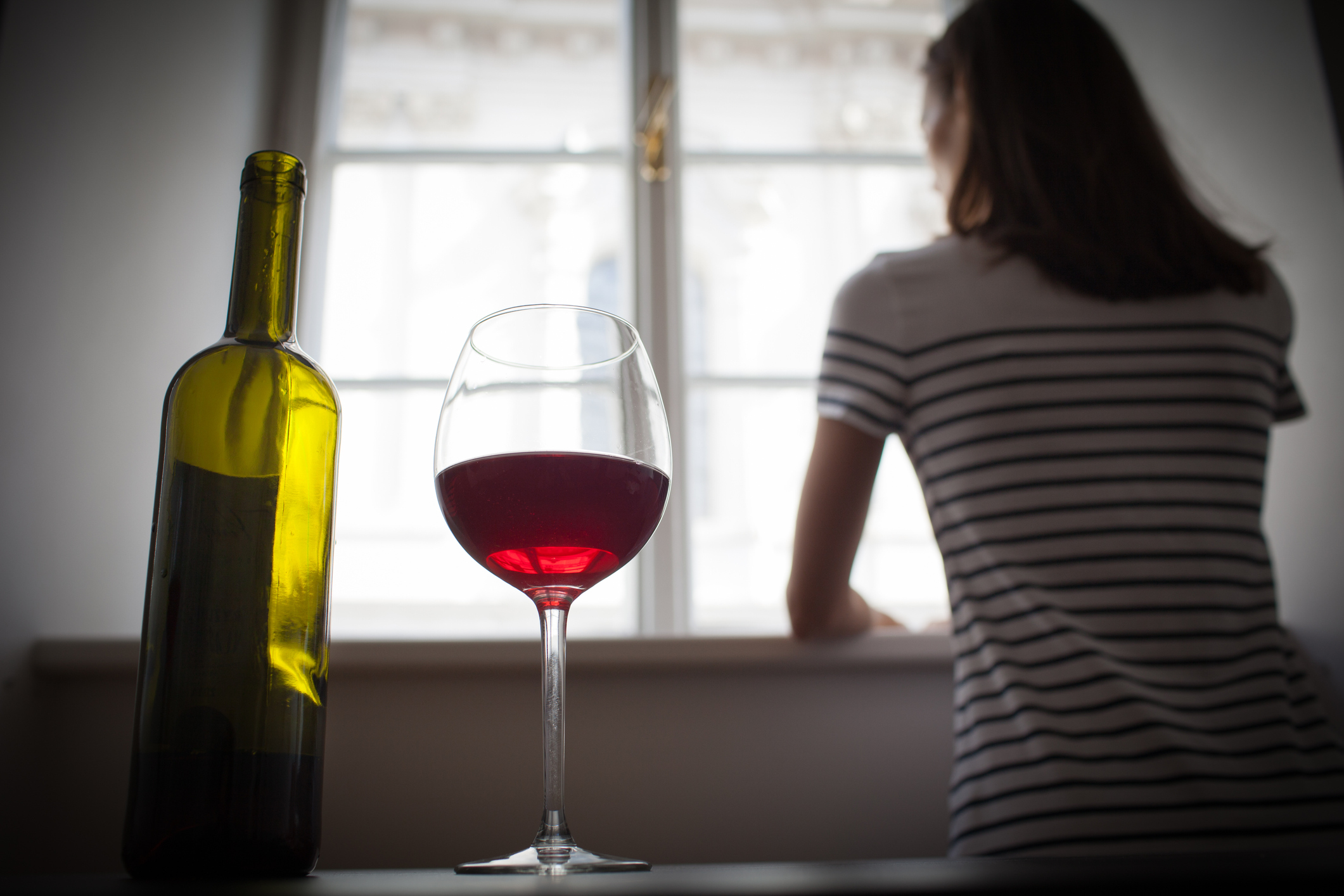 Person looks out of window with bottle and a glass of wine on a table