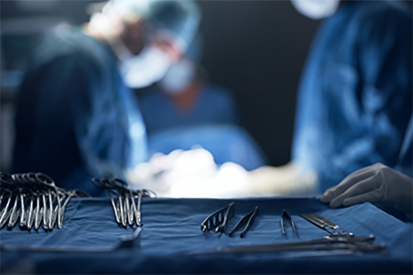 Closeup view of surgical tools on a tray while surgeons perform surgery in the background