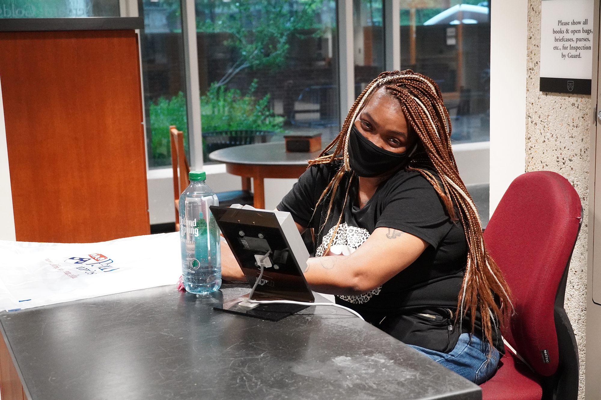 Angela Campbell wears a face mask and sits at a desk in the library foyer.