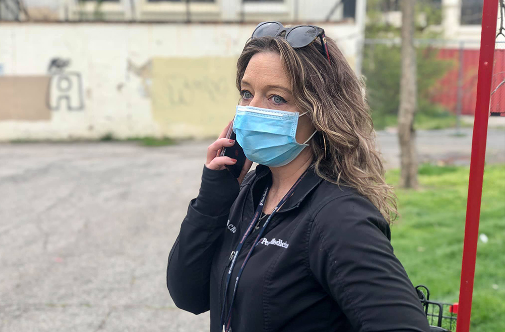 Nicole O’Donnell stands outside holding a smartphone to her ear while wearing a face mask. 