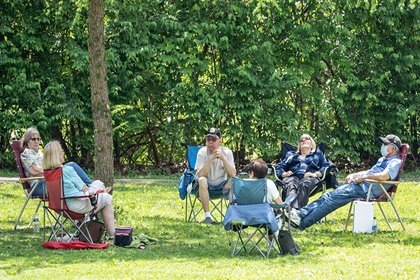 Six people sit socially distanced in folding camping chairs in a public park