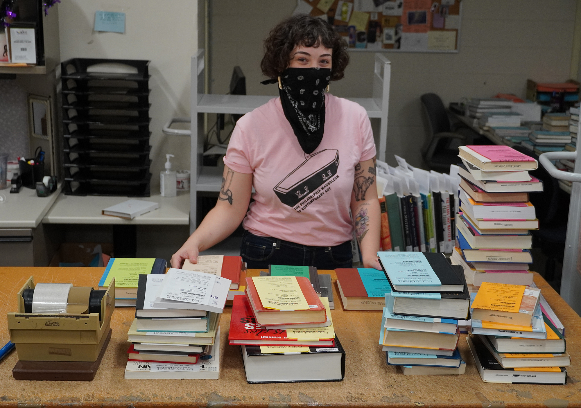 Jillian Richards wears a face mask standing at a desk of library books ready for checkout