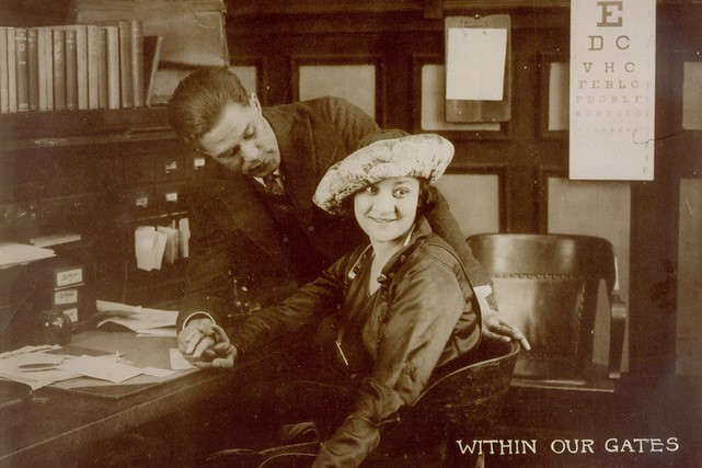 Two people dressed in clothing from the early 20th century at a desk in an office. 