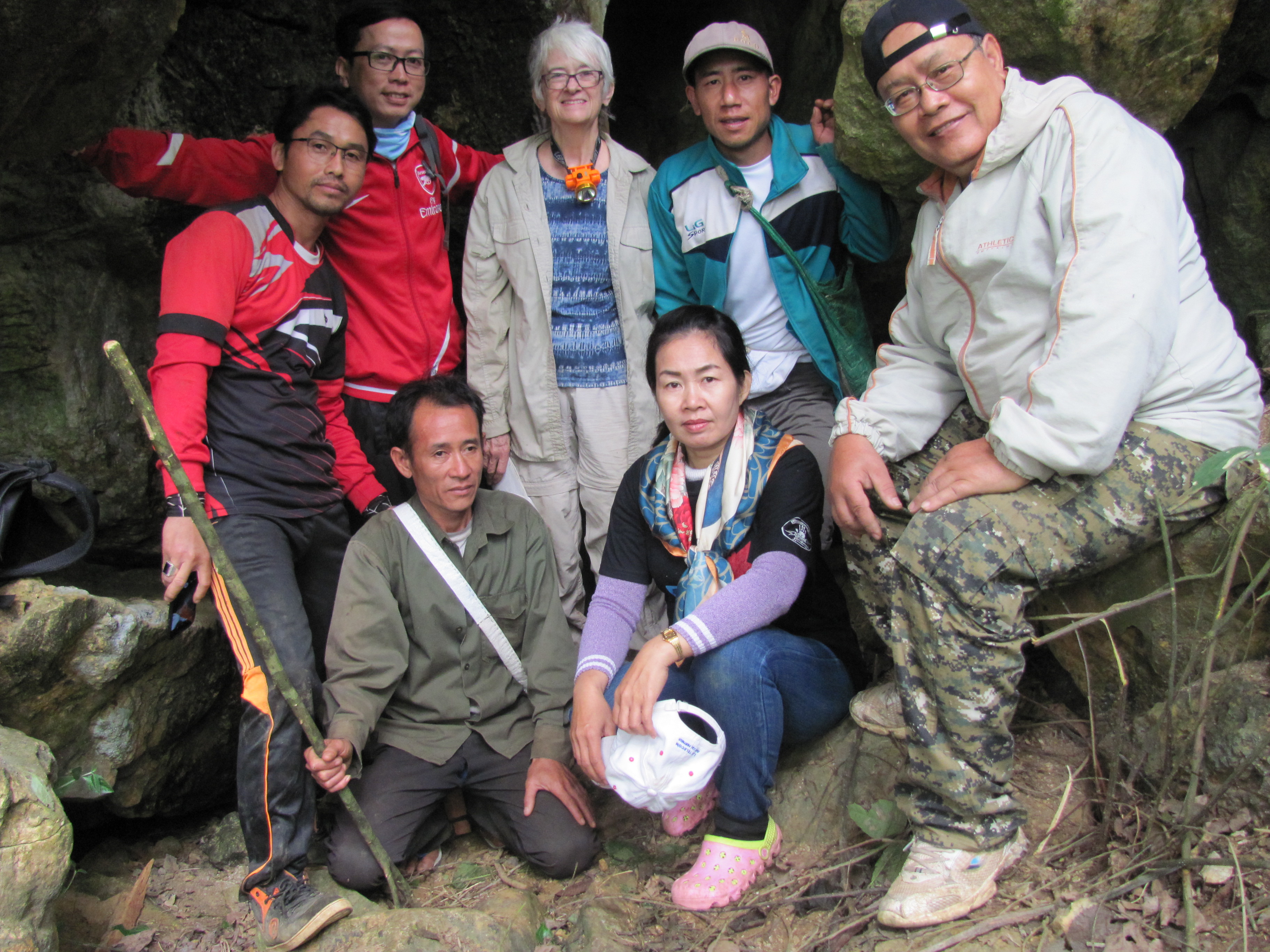 A group of archaeologists and excavators standing and sitting at the entrance of a cave. 