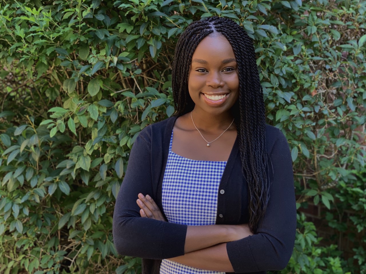 Student standing with arms crossed in front of foliage. 