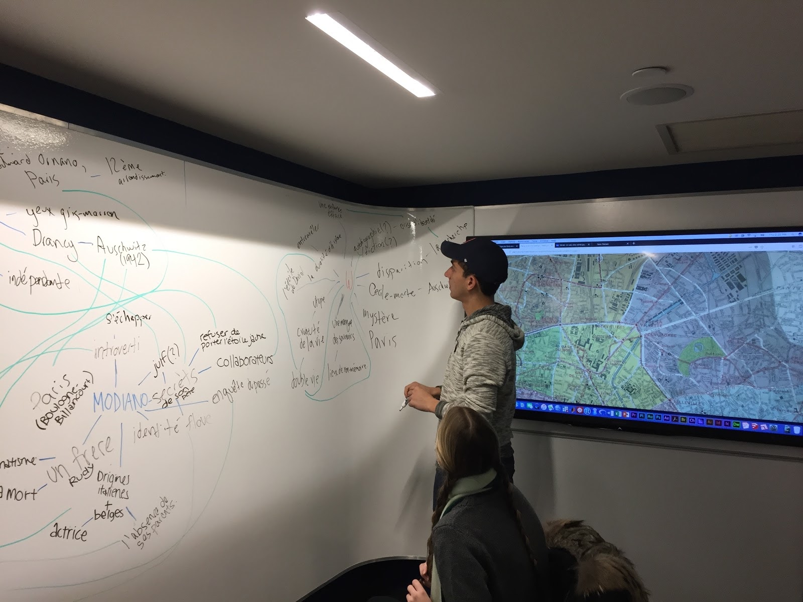 Person stands at a whiteboard covered in a word cloud, a map is projected on the wall beside them.