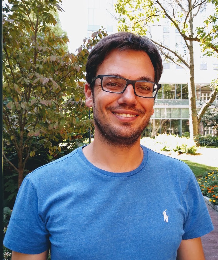 Smiling man in glasses poses in front of a building and foliage