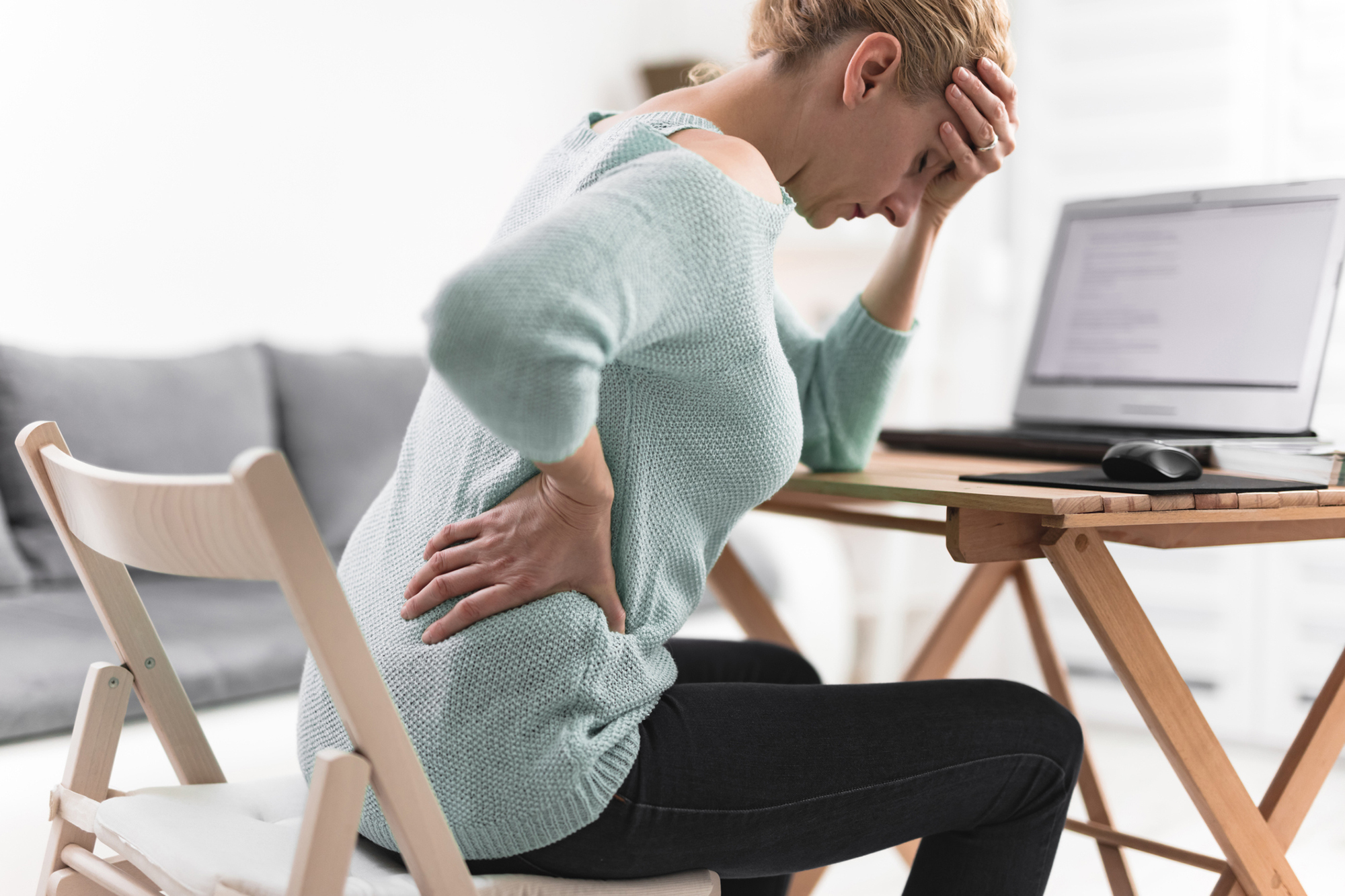 Person with back pain reaching for their back in a chair