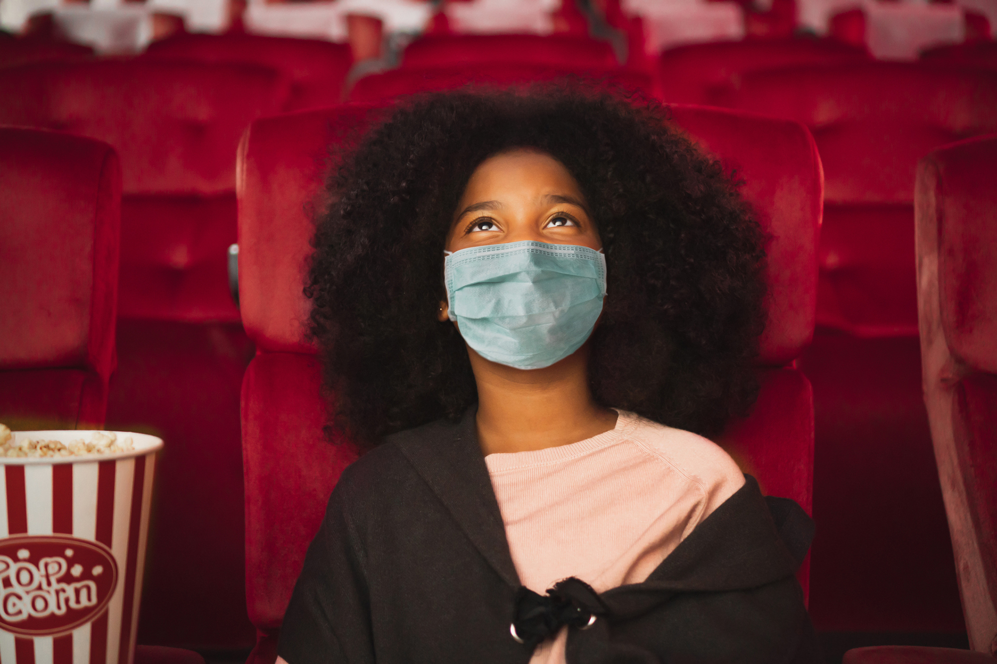 Young woman seated in theater with mask on 