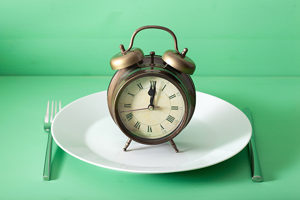 Old-fashioned alarm clock on top of an empty plate with a table setting
