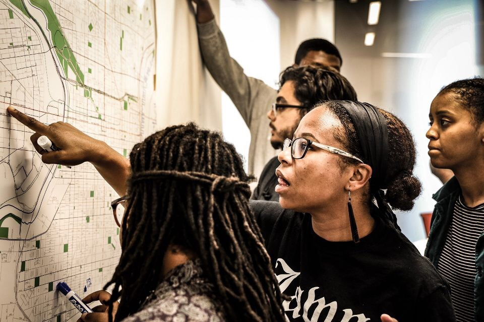 People standing at a large map posted on a wall, pointing at significant landmarks