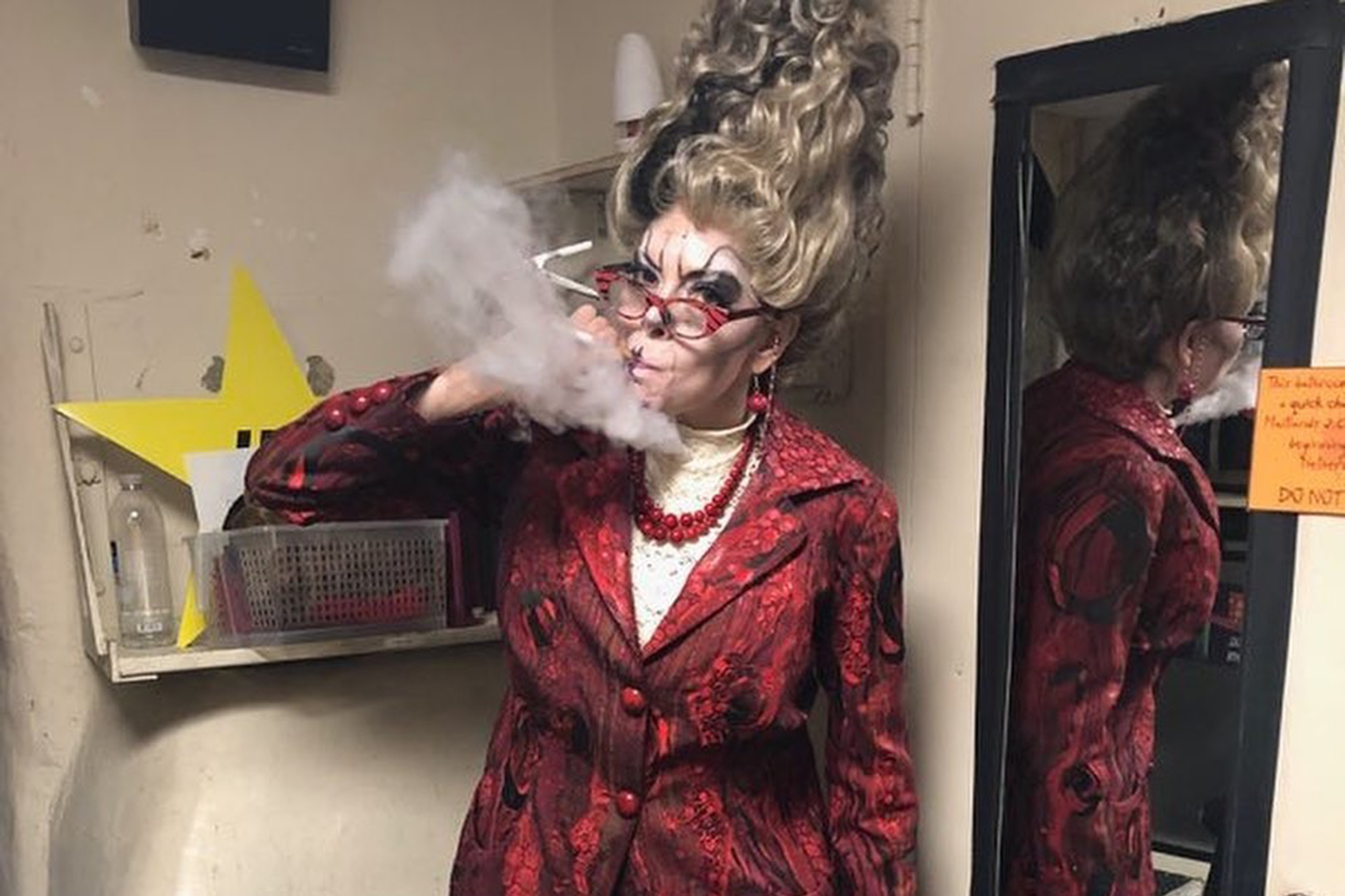 Smoking in theatrical costume with a red blazer and pearls