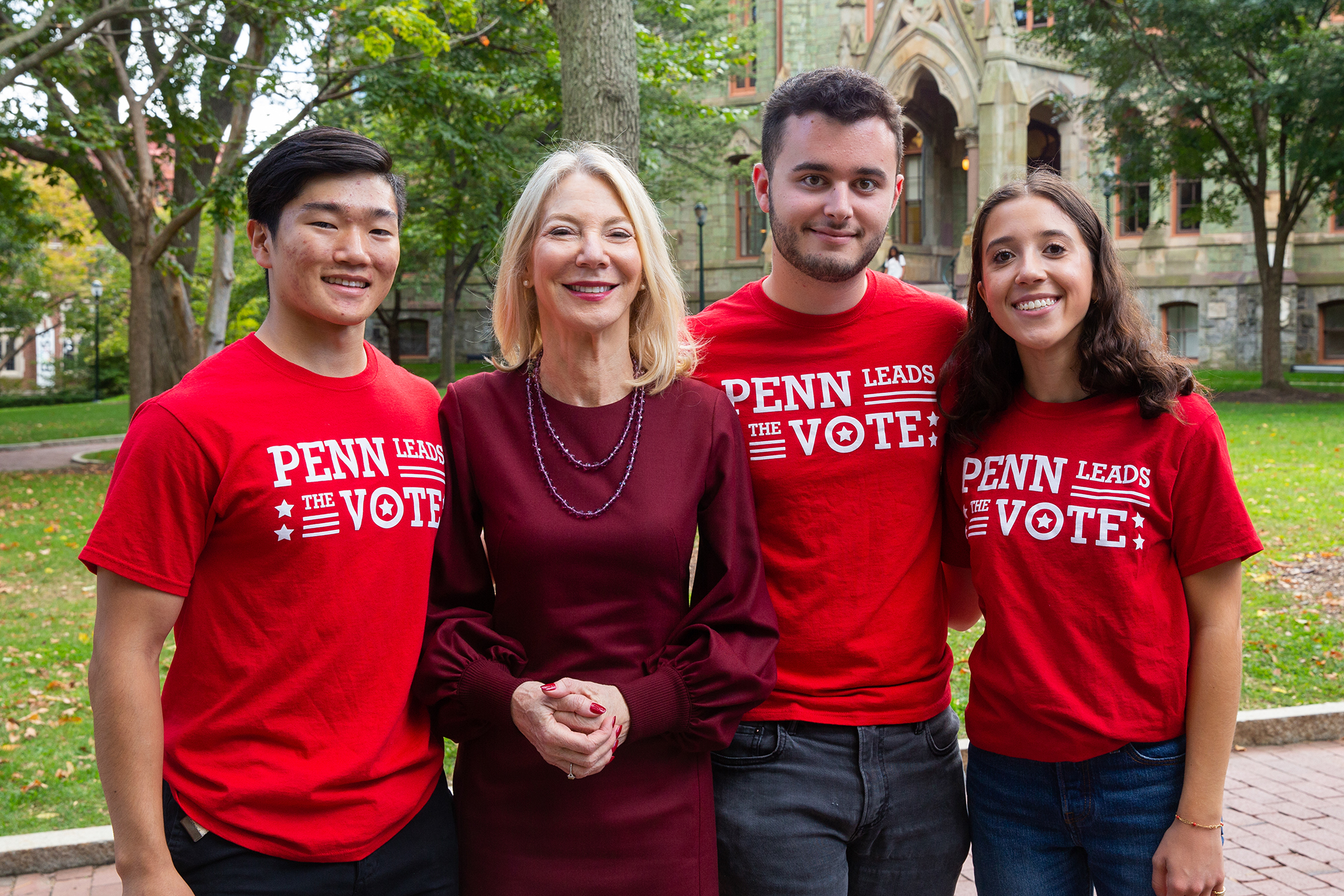 Four smiling people in front of College Hall; three wear "Penn Leads the Vote" t-shirts 