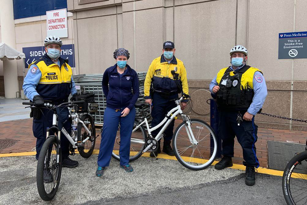 Penn DPS police officers wearing face-coverings standing with bikes in front building on campusa 