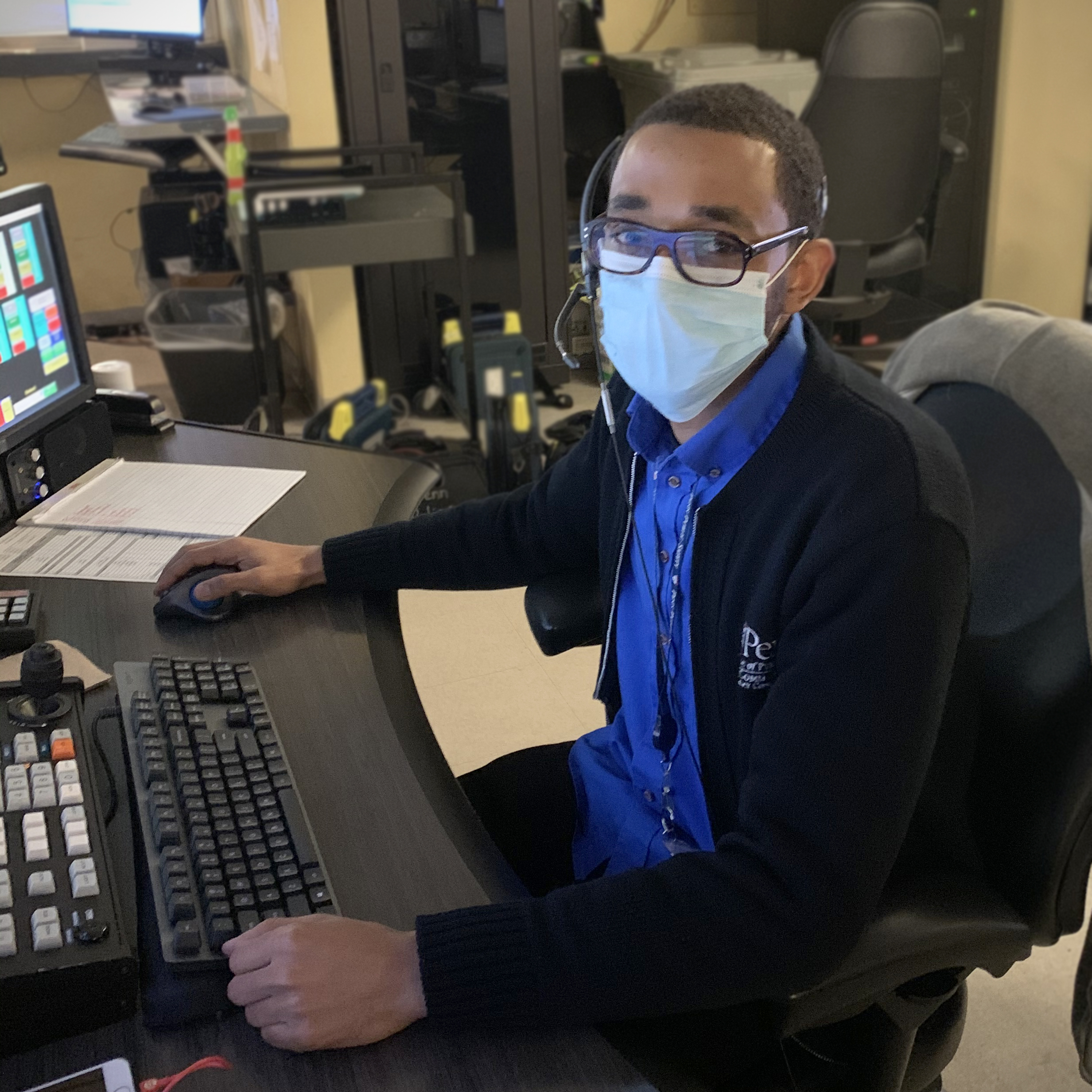 Dispatch photo of Johnathan sitting at desk fielding calls wearing a face covering